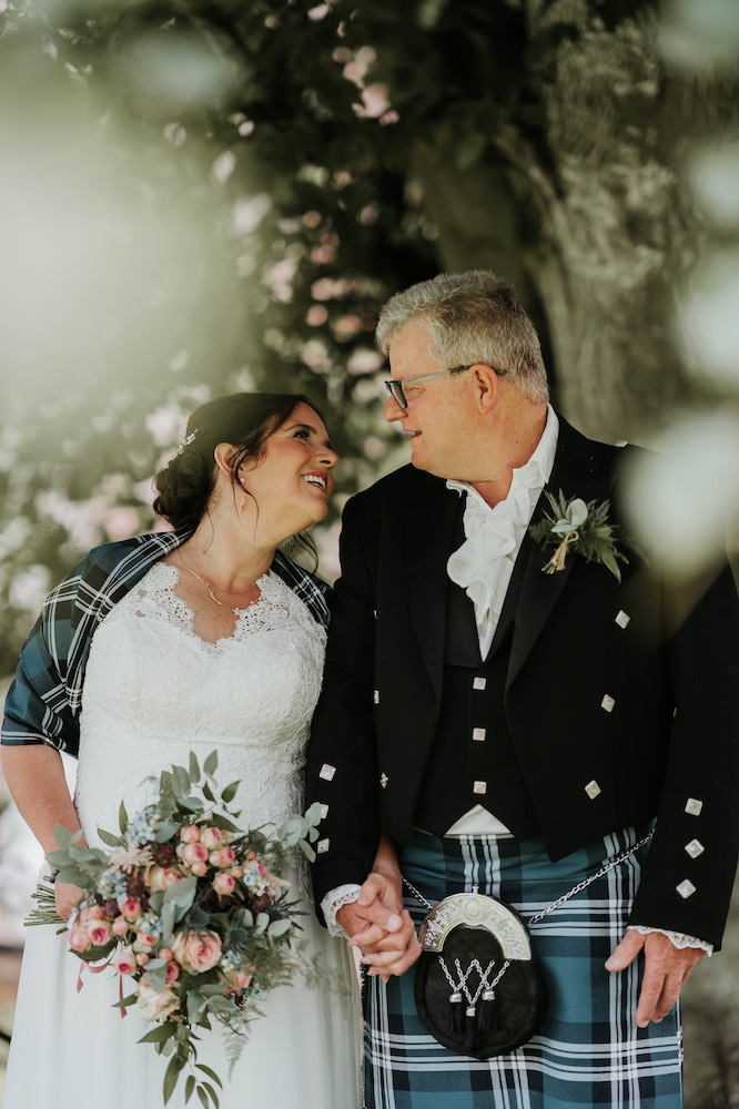 Ein Brautpaar in Hochland-Tracht mit Kilt und Kleid schaut sich verliebt in die Augen.